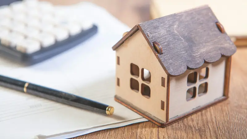 Calculator, fountain pen and papers on a wooden desk beside a small wooden model house
