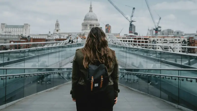Woman with a backpack seen from behind walking across the Millennium Bridge in London towards St Paul's Cathedral