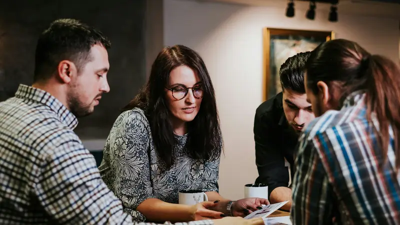 Four colleagues gathered round a table looking at printed papers together, a woman in glasses in the middle